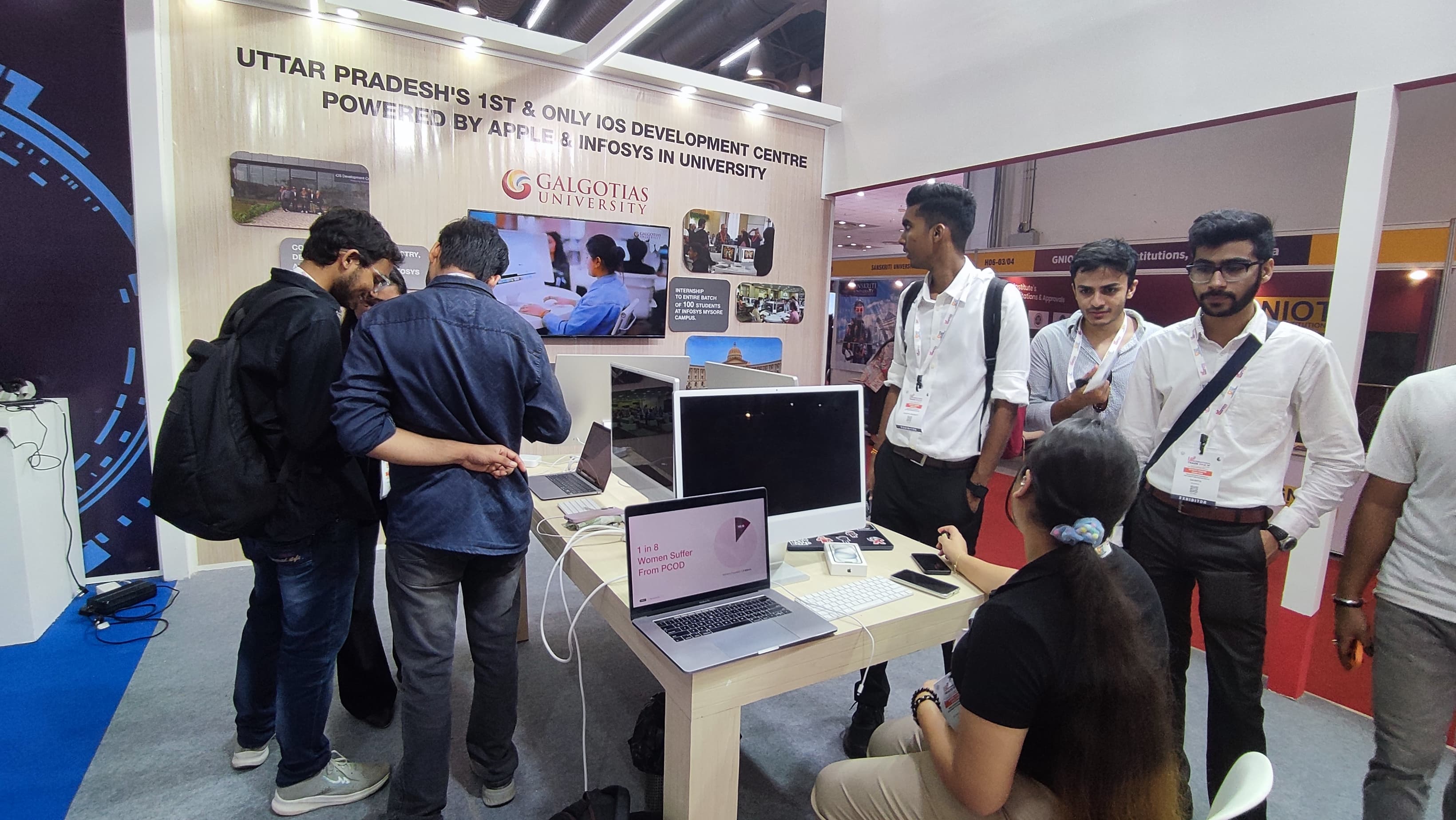 Team Sakhi's exhibition booth at a technology showcase, under a banner reading Uttar Pradesh's 1st and only iOS Development Centre powered by Apple and Infosys in university, with the Sakhi app open on a laptop