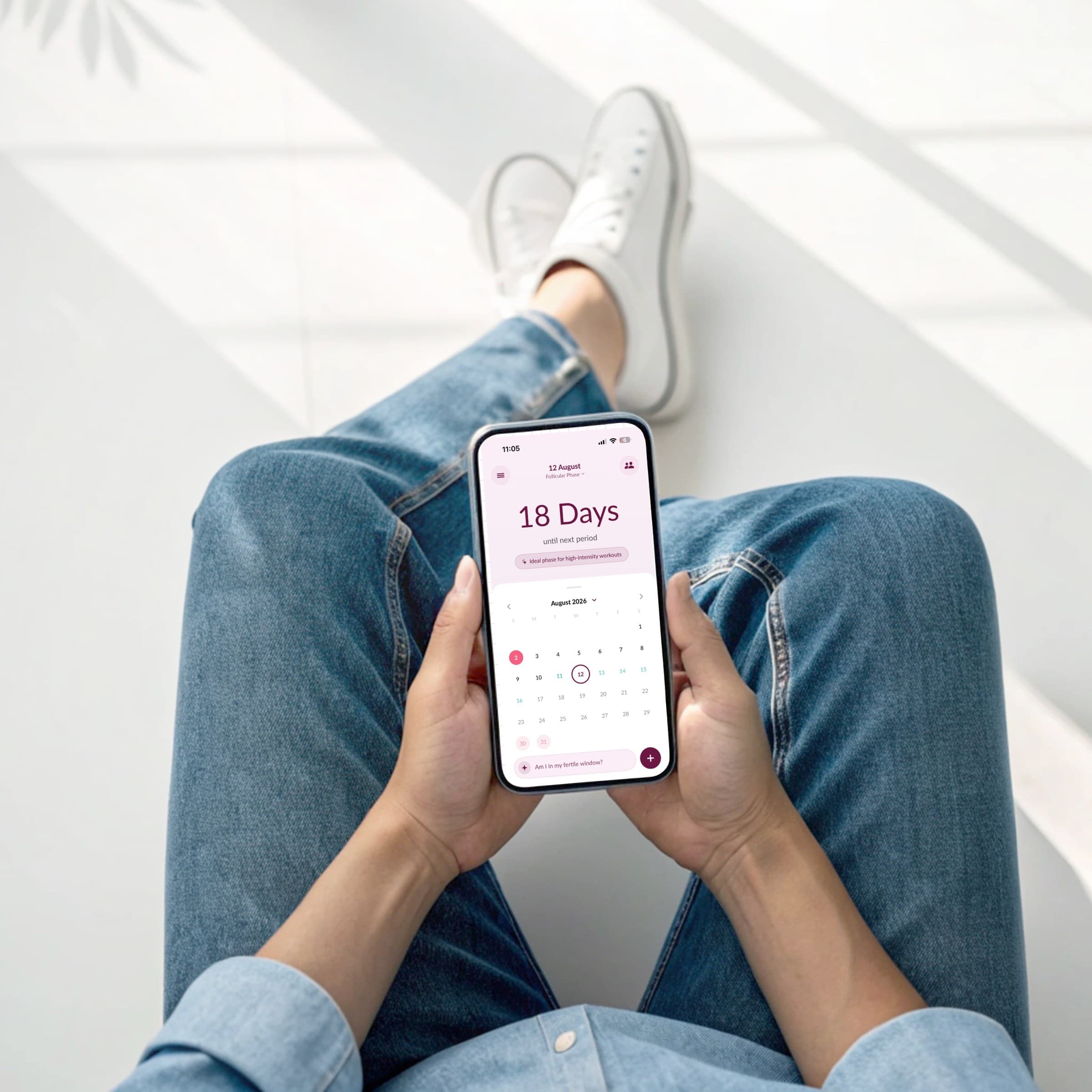 Overhead view of a woman holding the Sakhi app, showing 18 days until her next period and the August calendar