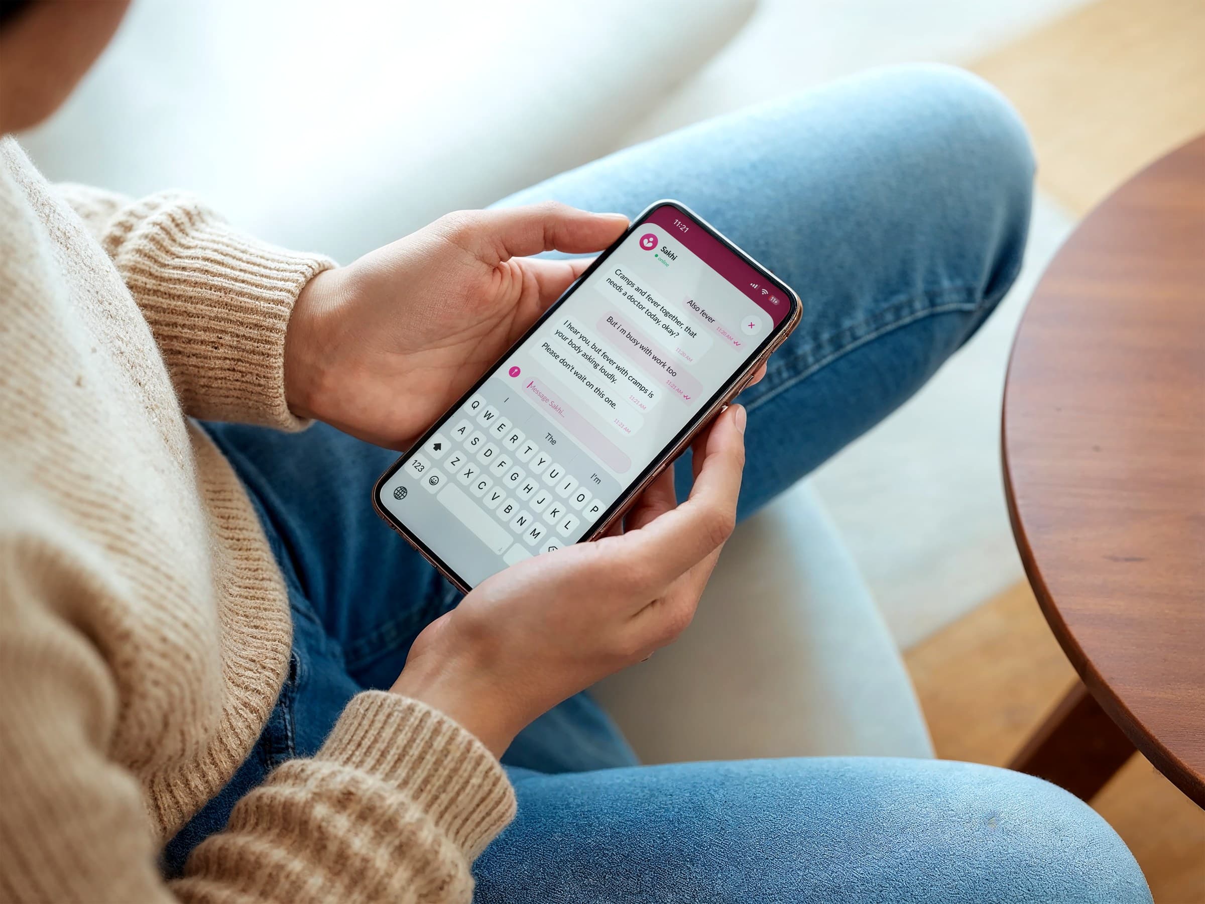 A woman typing a message to Sakhi about cramps and a fever, and being told to see a doctor today